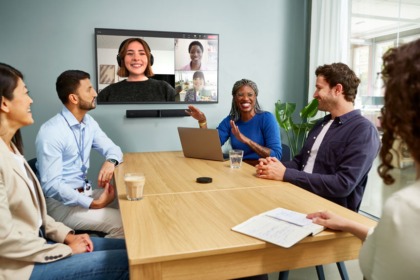 An image of a group of 5 workers chatting on a video conference call with three on screen colleagues using the Jabra PanaCast 50 video conferencing unit.