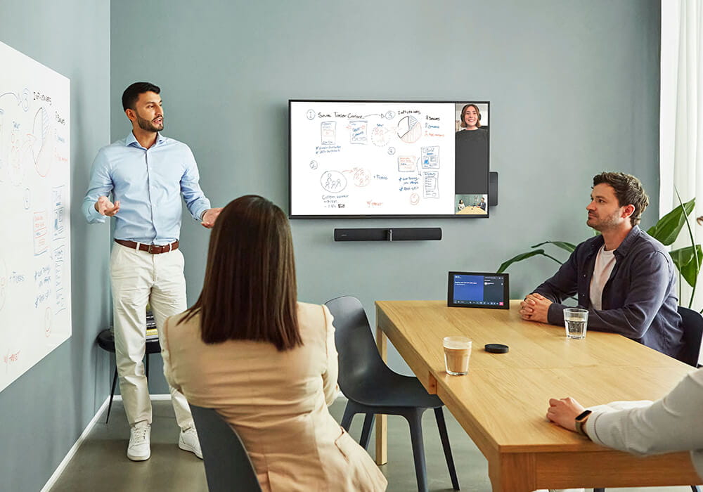 An image of a PanaCast 50 Room System being used in a video conferencing room with four workers, the screen displays a close up of the whiteboard in the room using the whiteboard sharing feature.