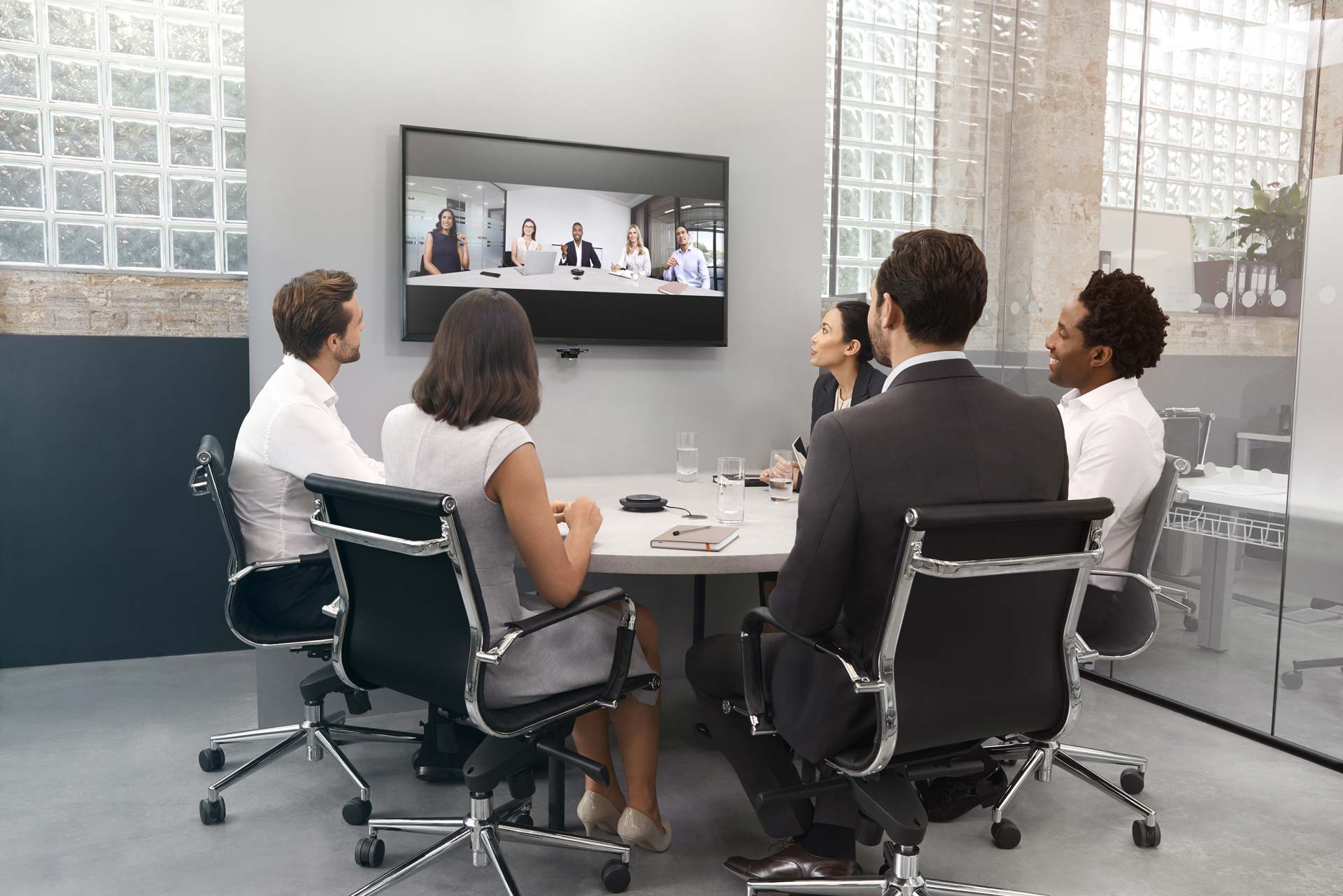 An image of a full huddle room with five workers video conferencing in front of the PanaCast camera with a Jabra Speak 750 conferencing speaker.